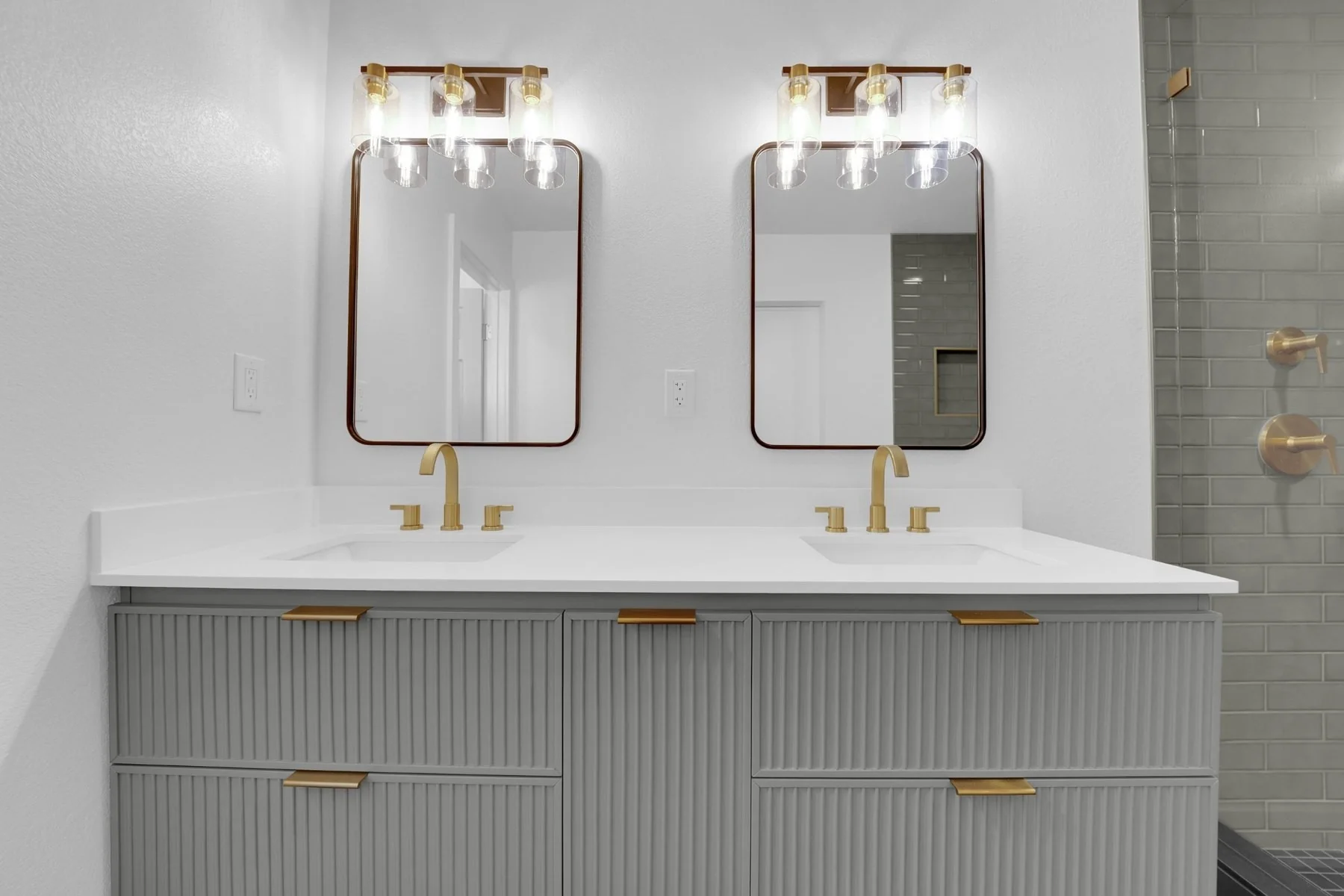 Front view of gray fluted double vanity with white countertop, dual sinks, gold hardware, and framed mirrors