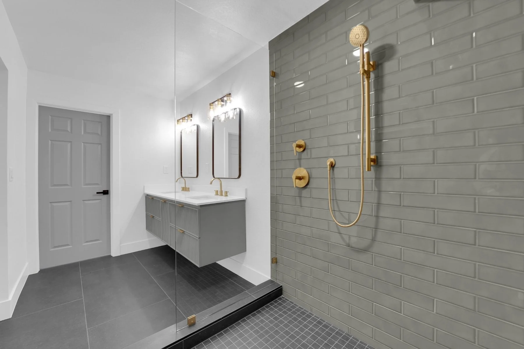 View from the green tile shower toward the floating gray double vanity and remodeled bathroom entrance