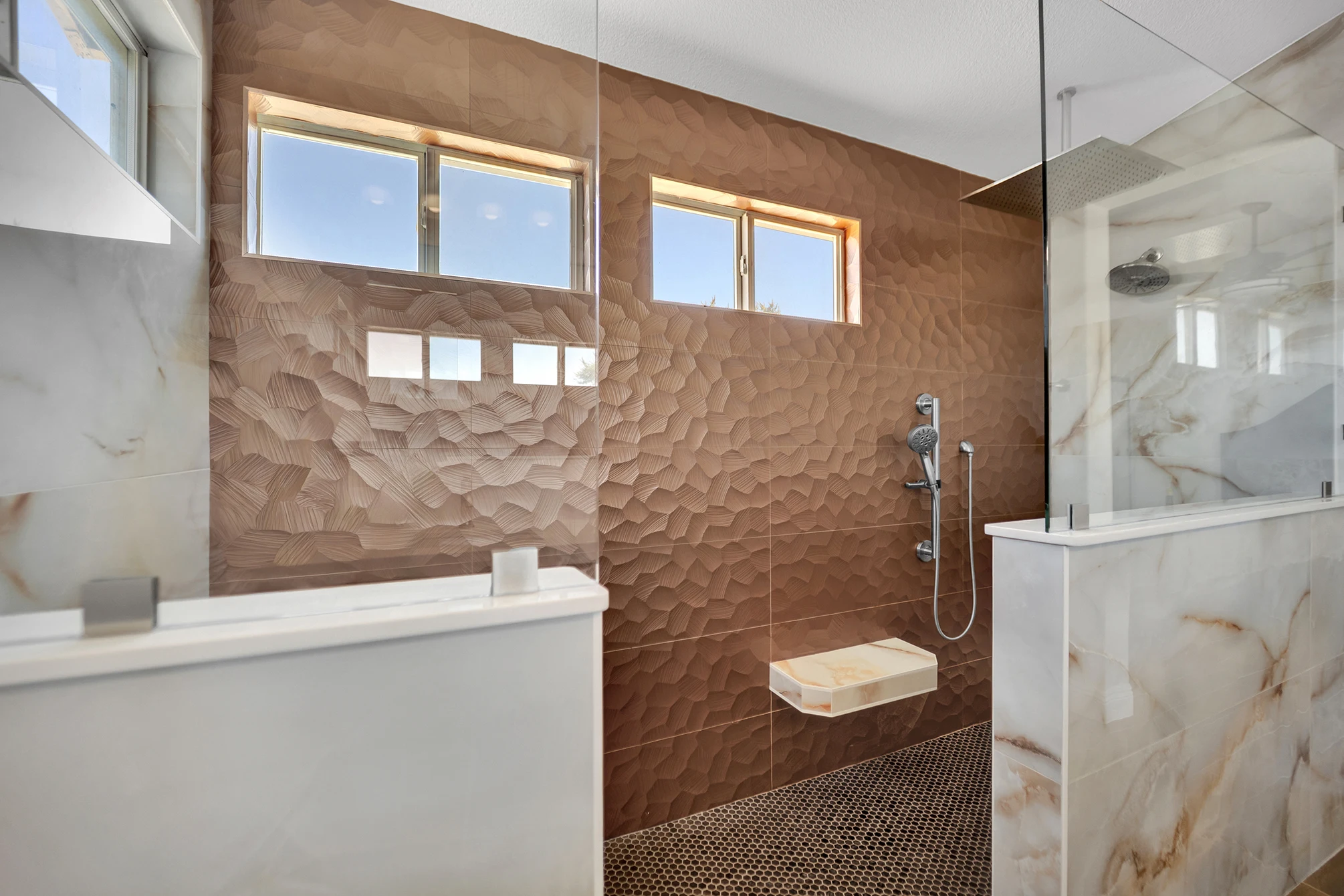 Copper-tone shower accent wall beneath high windows, with floating seat, handheld shower and penny mosaic floor.