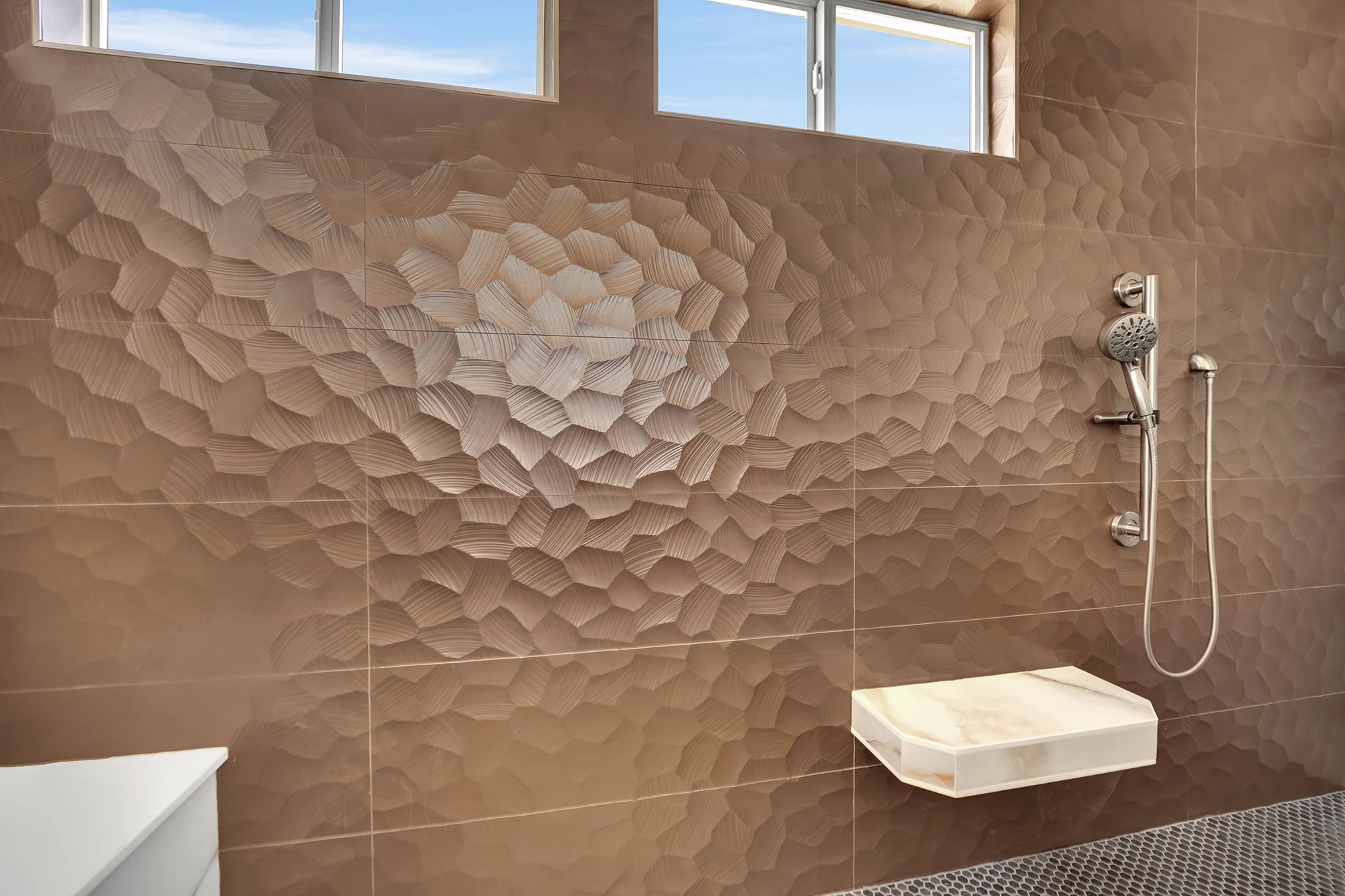 Close view of copper-tone textured shower tile with a floating veined seat and Kohler handheld shower.