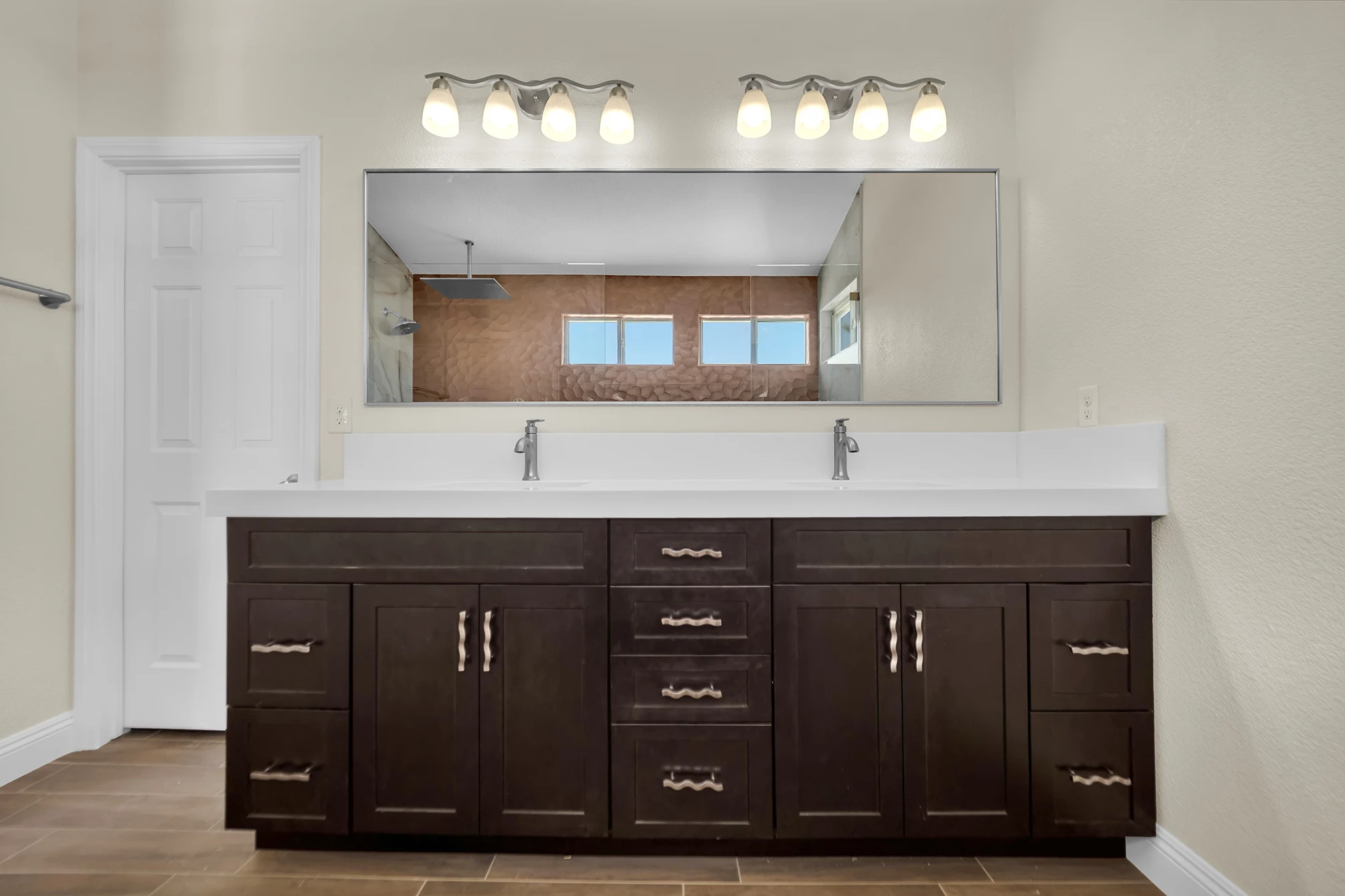 New dark double vanity with white countertop, wide mirror and two four-light fixtures in the remodeled bathroom.