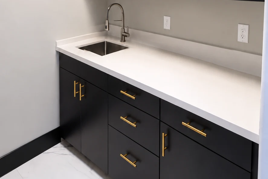 Dark custom office base cabinets with gold-colored pulls, a light countertop, sink, and drawers.