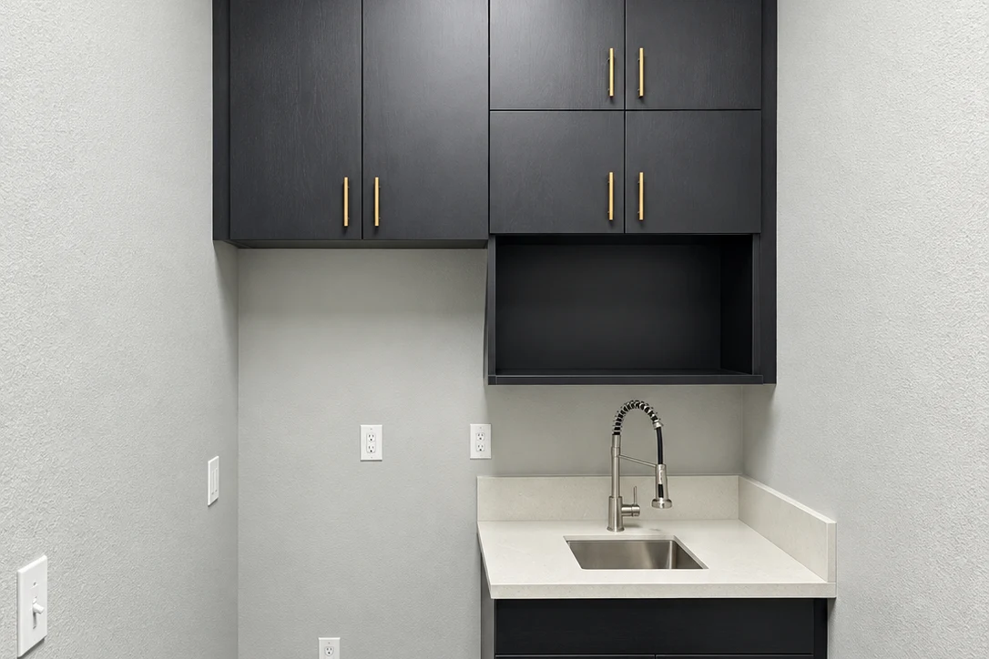 Compact cabinet-and-sink area with tall dark upper cabinets, gold-colored pulls, an open cubby, and a light countertop.