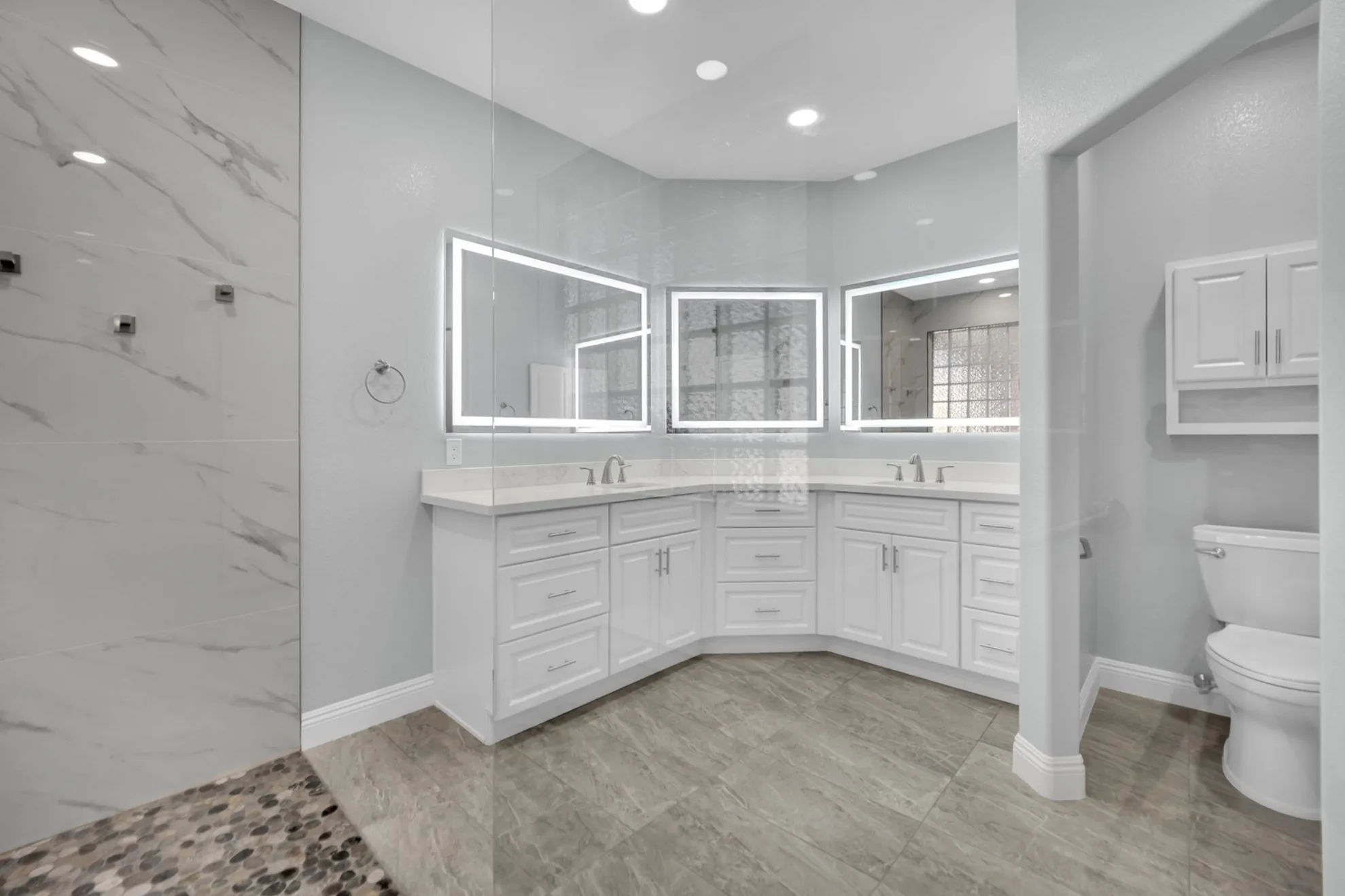 Semi-custom white shaker vanity with prefabricated quartz top and lighted mirrors in a bathroom remodel