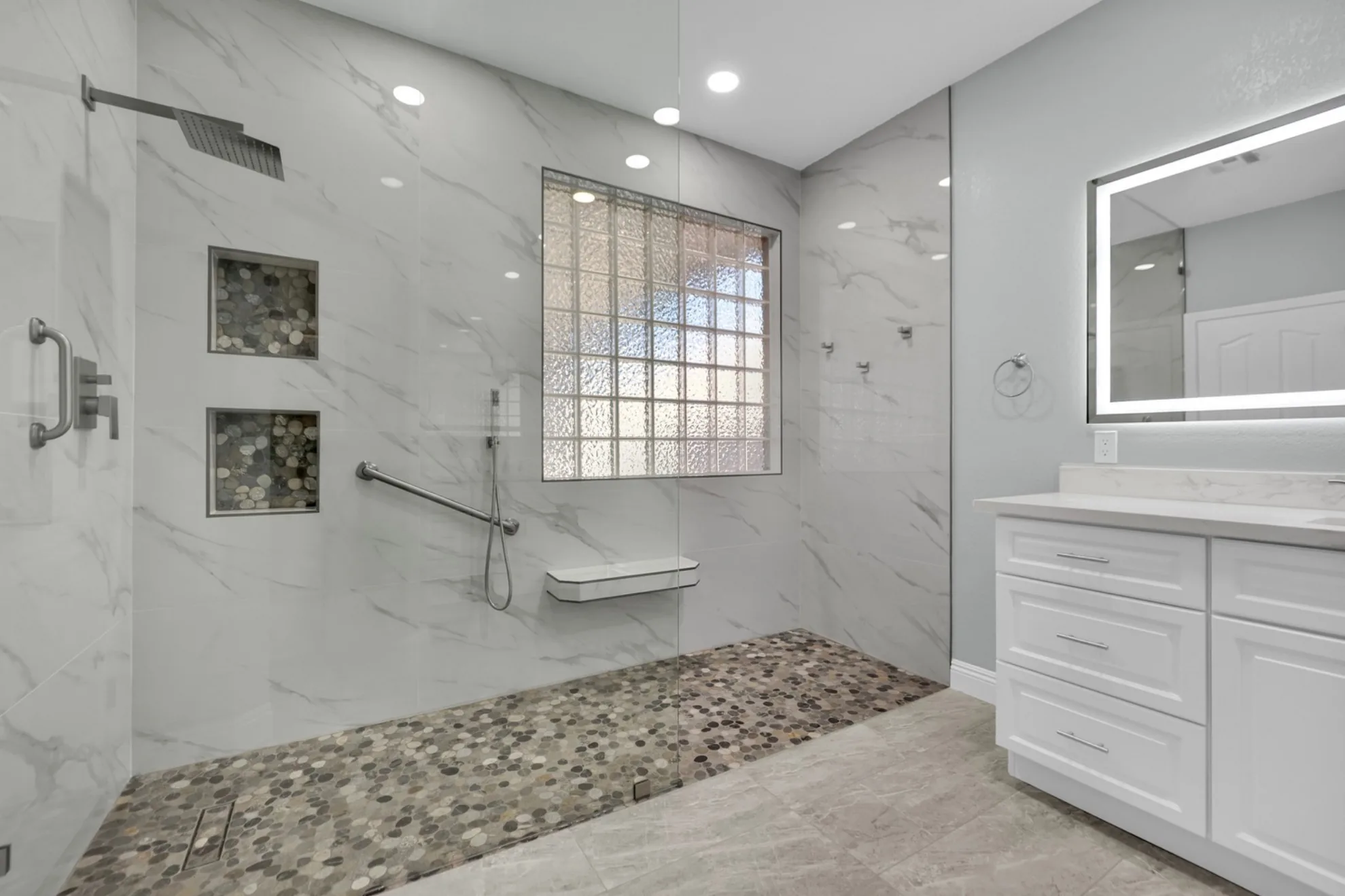 Finished curbless shower with linear drain, glass block window, grab bars, and marble-look porcelain tile
