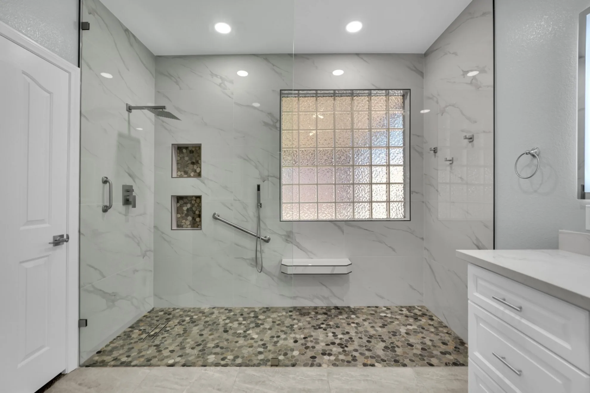 Curbless walk-in shower with floor-to-ceiling fixed glass panel and pebble tile floor