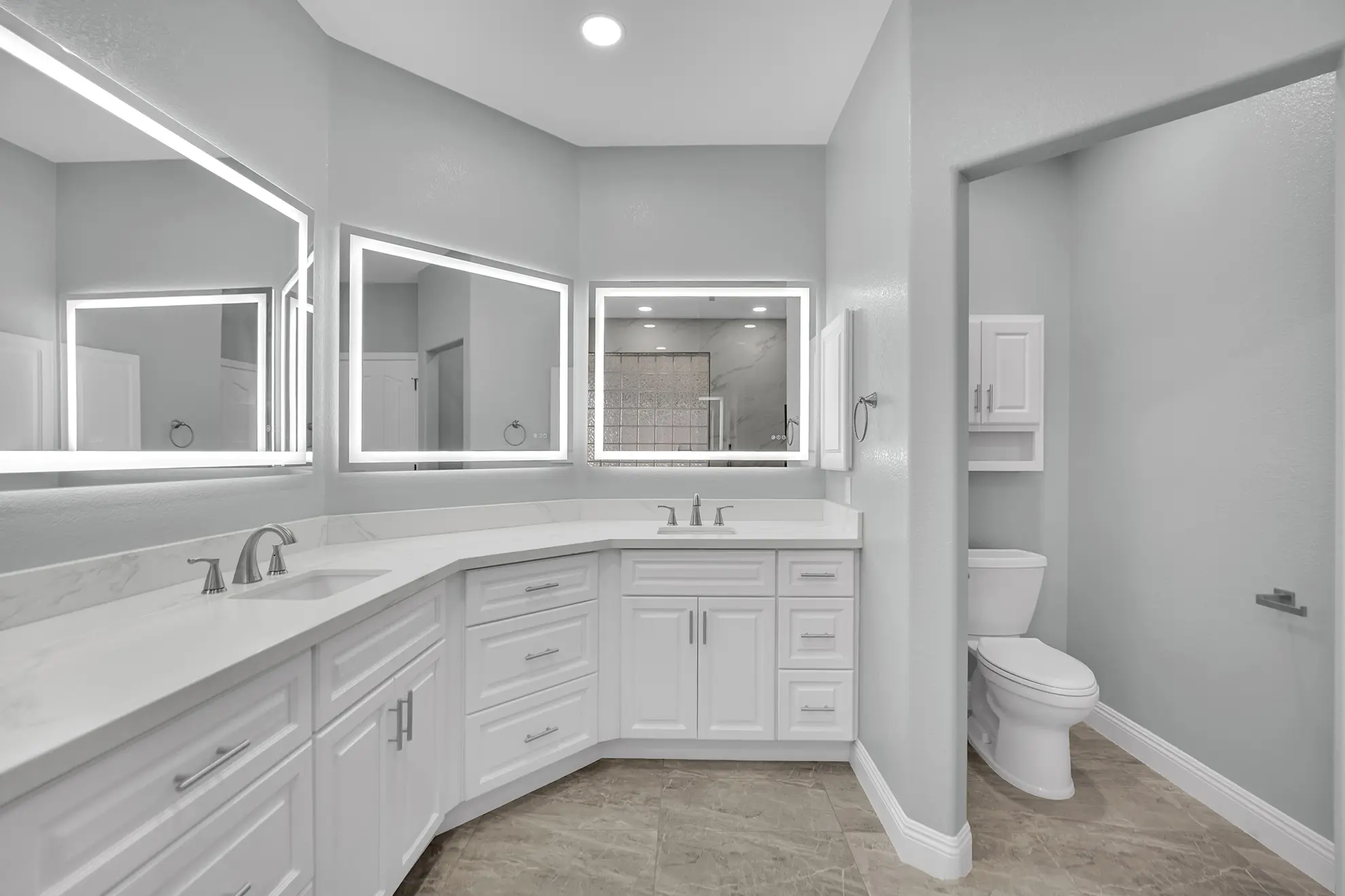 Wide view of the bathroom remodel with white shaker vanity, lighted mirrors, toilet area, quartz countertop, and shower reflected in the mirror