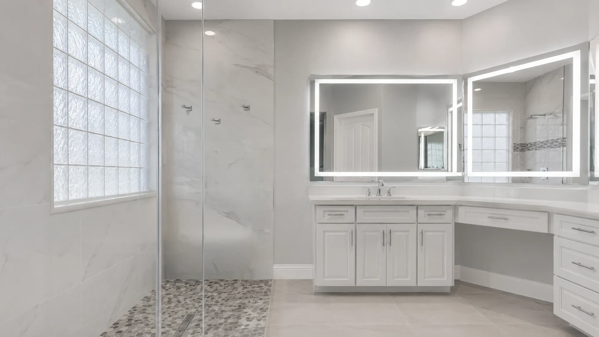 Finished bathroom after the curbless walk-in shower conversion with fixed glass, pebble floor, grab bars, white vanity, and lighted mirrors