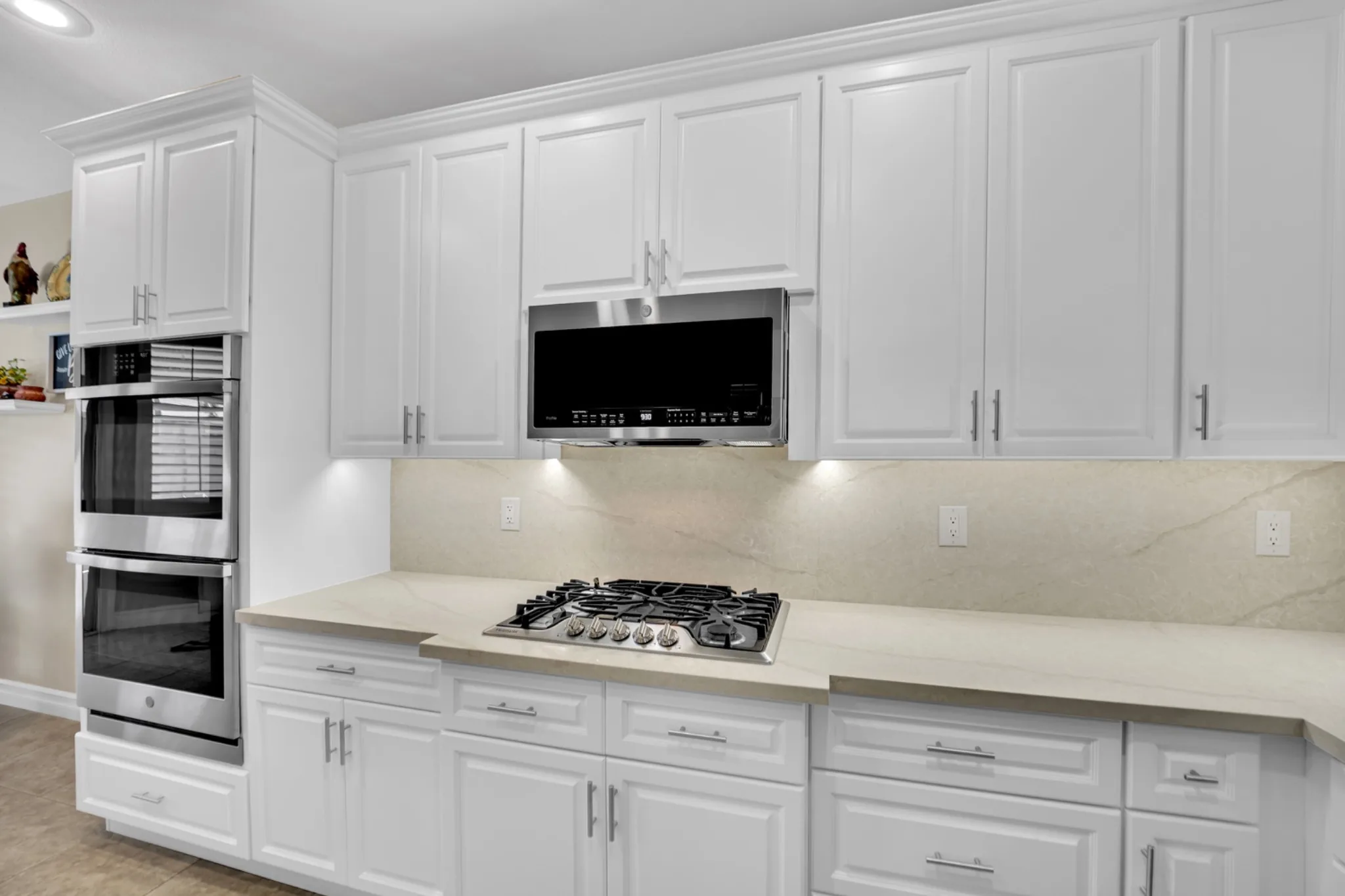 White raised-panel cabinets with matching quartz backsplash, new stainless appliances, and retained tile flooring