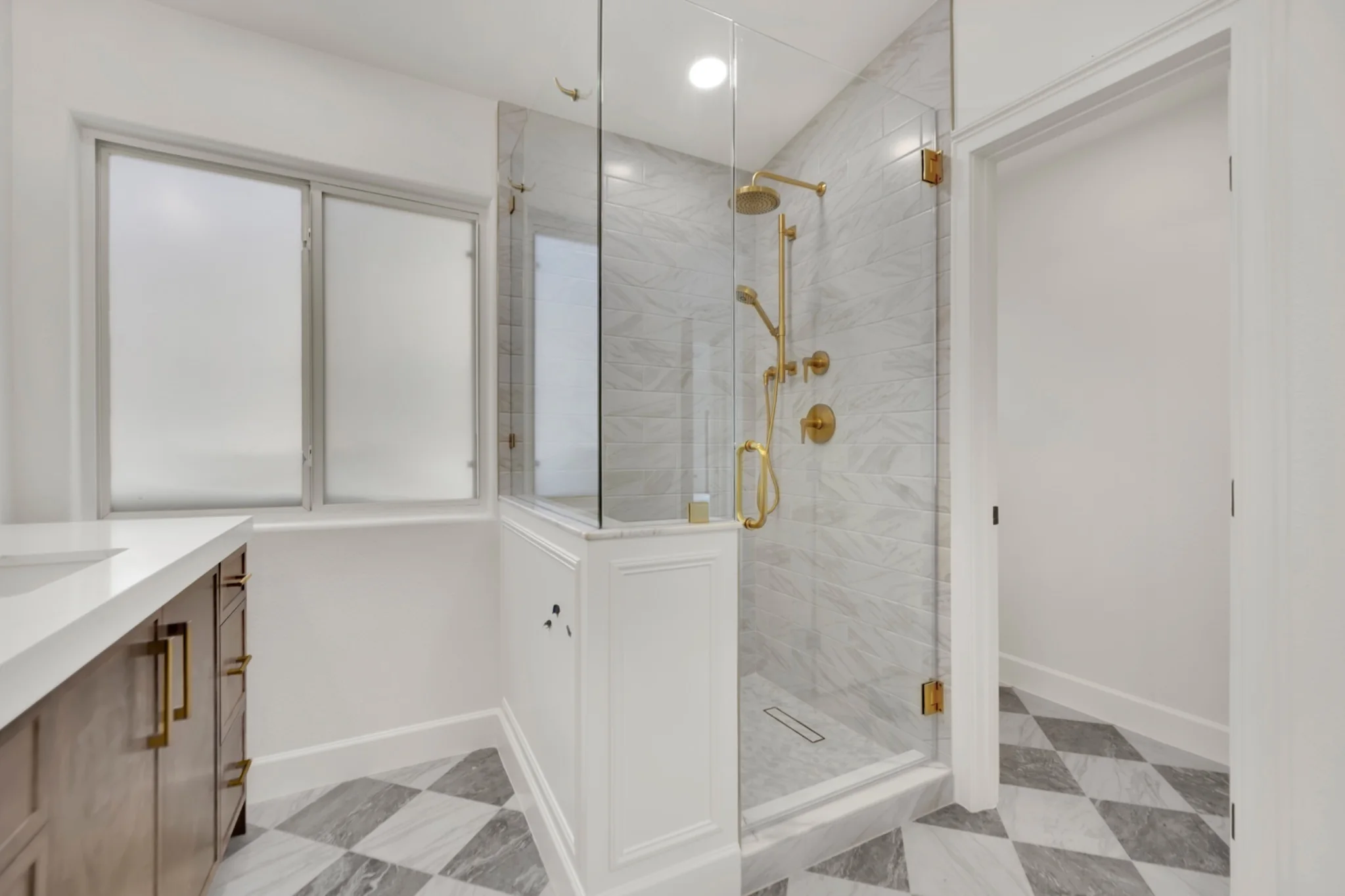 Custom marble shower with gold fixtures, tile-in drain, and glass enclosure