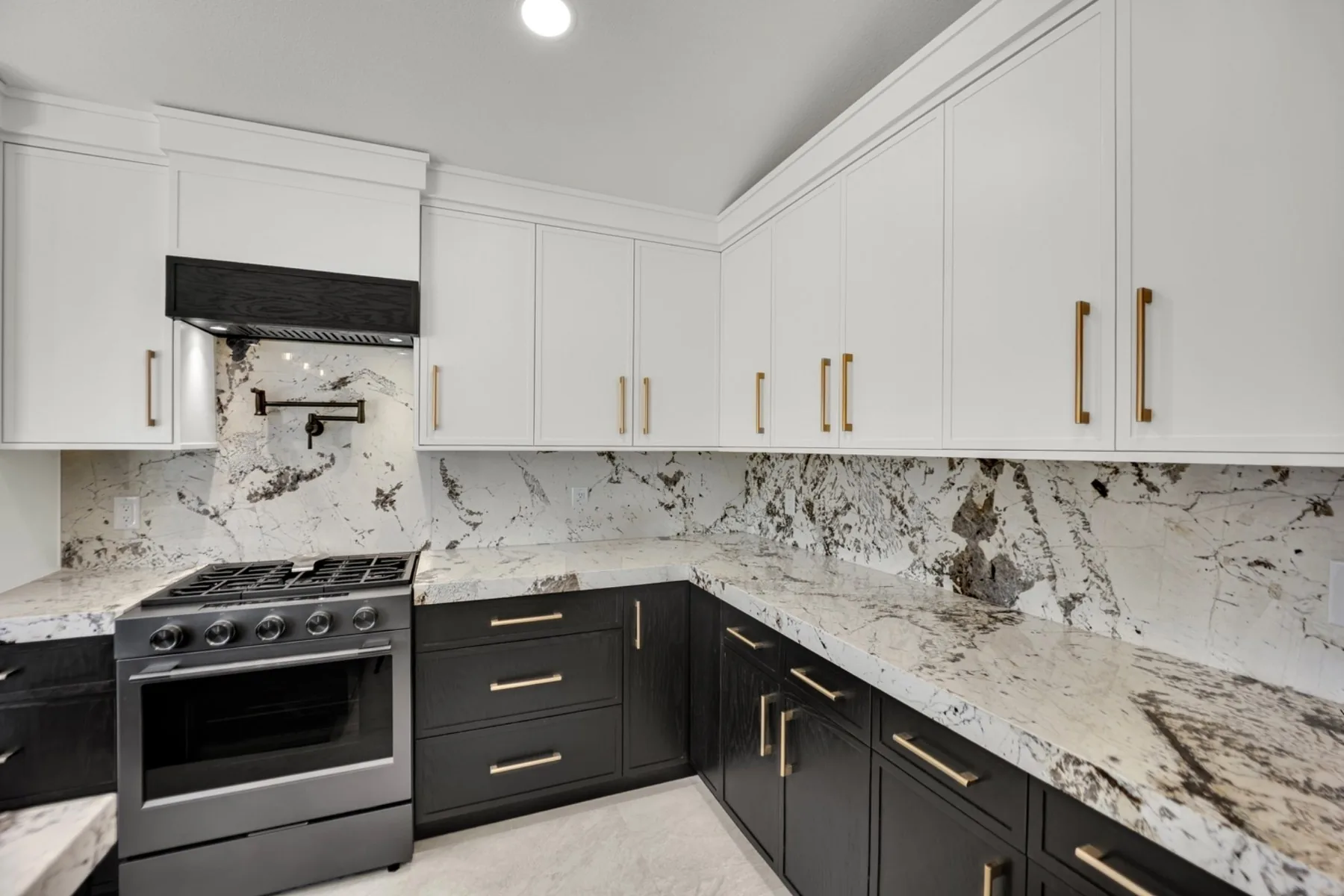 Granite slab backsplash and range wall with cream upper cabinets and dark painted lower cabinets in Summerlin kitchen