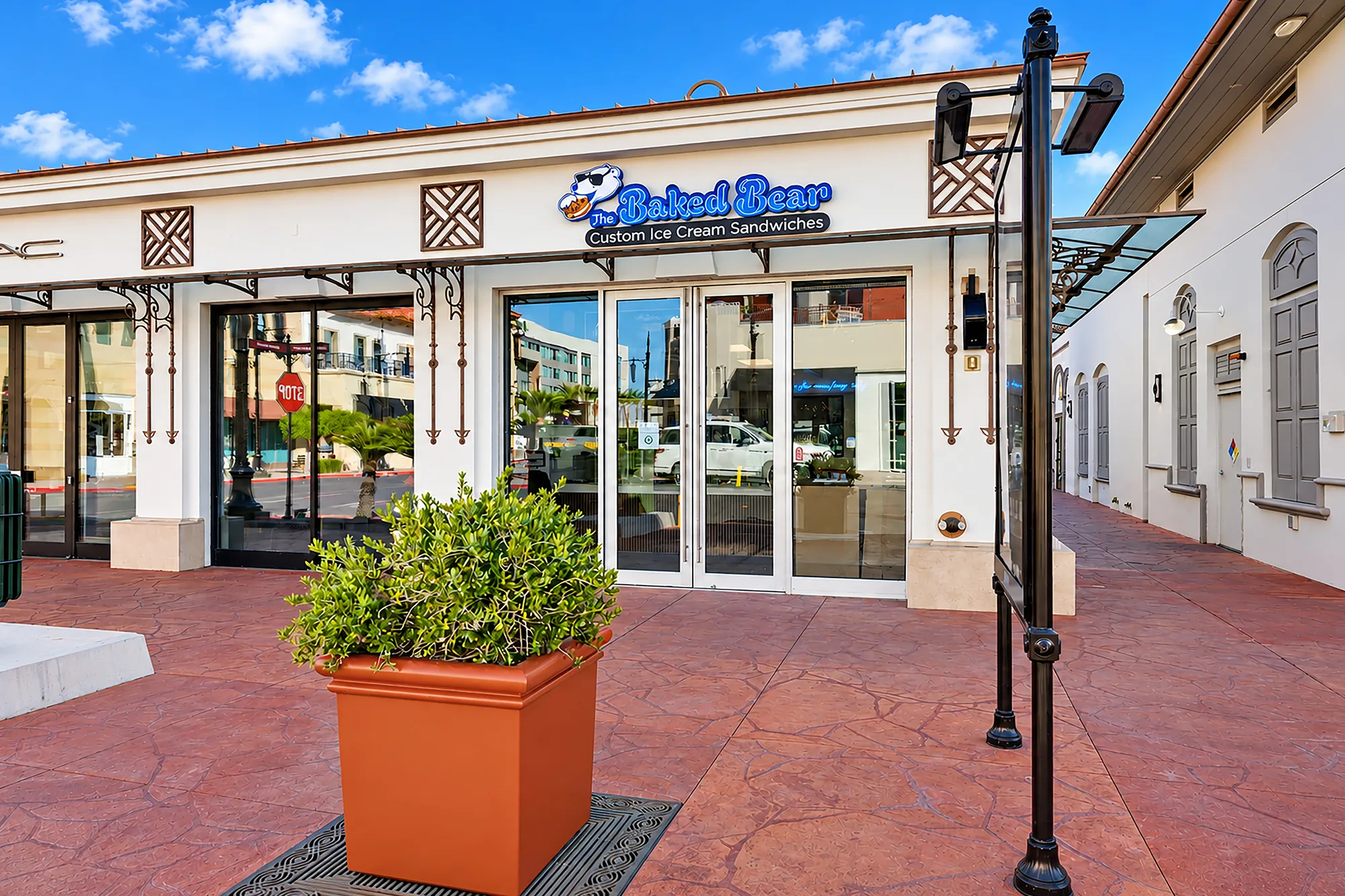 The Baked Bear storefront viewed from the walkway behind a planter and black lamp post.